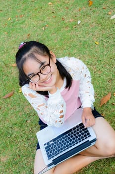Lovely girl is happy with a laptop on lawn in park