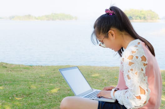 Young girl with laptop on the grass by the lake in park