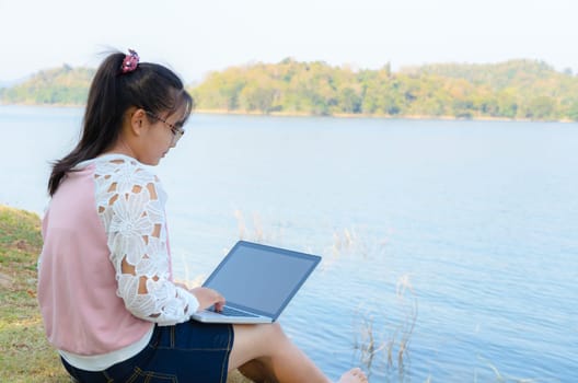 Young girl with laptop sitting on the riverbank  in park