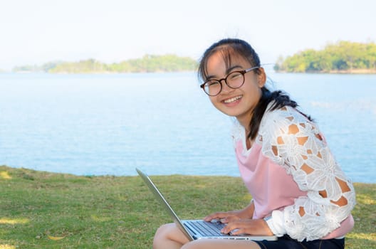 Young girl with laptop on the grass by the lake in park
