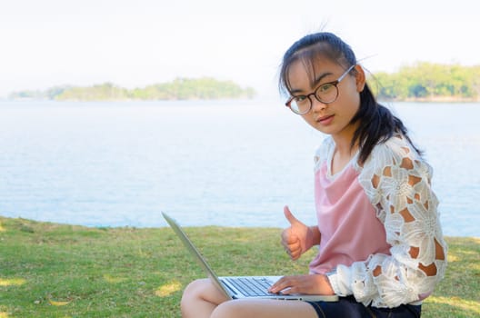 Young girl with laptop on the grass by the lake in park