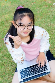 Lovely girl is happy with a laptop on lawn in park