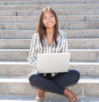 Beautiful asian girl sitting on stairs and using a laptop