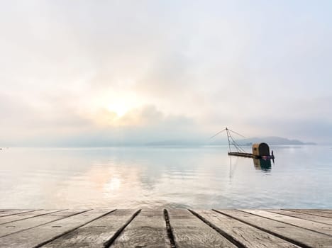 Morning concept with boat on lake with sunlight and dramatic sky, focus on wooden desk.