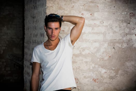 Handsome young man in old building against brick wall, looking at camera