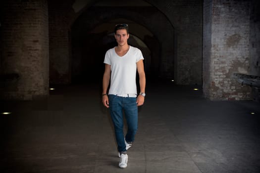 Handsome young man in old building walking inside gallery, looking at camera, full figure shot