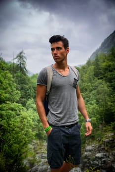 Handsome muscular young man backpacking or hiking in lush green mountain scenery pausing to look at something  far away