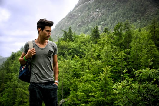 Handsome muscular young man backpacking or hiking in lush green mountain scenery pausing to look at something  on the ground