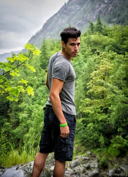 Handsome muscular young man hiking in lush green mountain scenery looking at camera