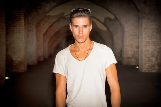 Handsome young man in old building walking inside gallery, looking at camera