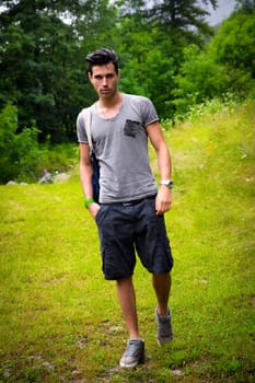 Handsome muscular young man backpacking or hiking in lush green mountain scenery looking at camera