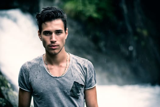 Handsome young man near mountain waterfall looking at camera