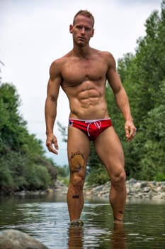 Handsome young muscle man standing in water pond, naked wearing only bathing suit