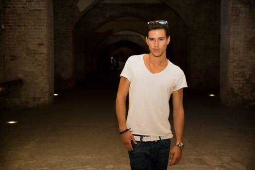 Handsome young man in old building walking inside gallery, looking at camera