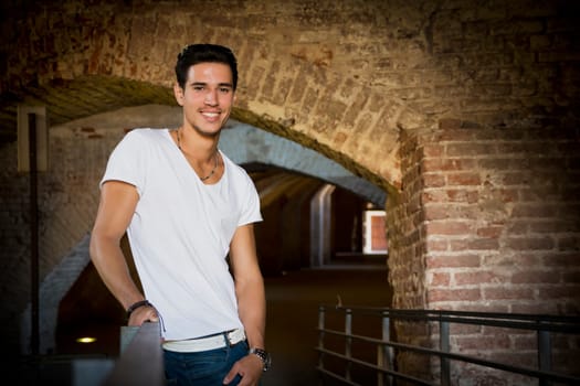 Handsome young man in old building leaning on handrail, smiling and looking at camera