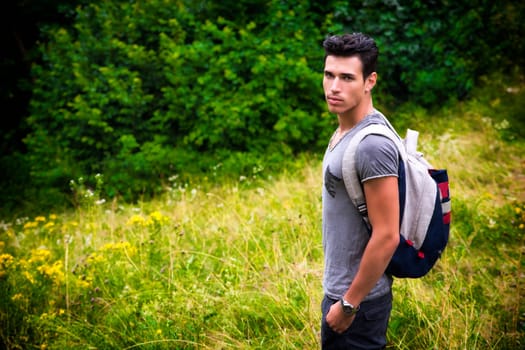 Handsome muscular young man backpacking or hiking in lush green mountain scenery looking at camera