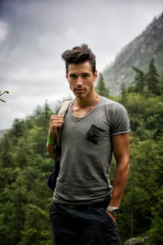 Handsome muscular young man backpacking or hiking in lush green mountain scenery looking at camera