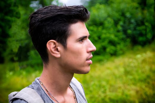 Handsome muscular young man backpacking or hiking in lush green mountain scenery looking away