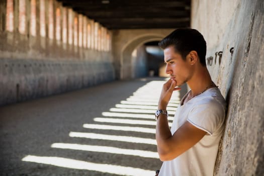 Handsome young man in old building against brick wall, looking down
