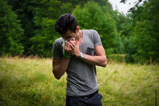 Young man outdoors sneezing in handkerchief, blowing his nose