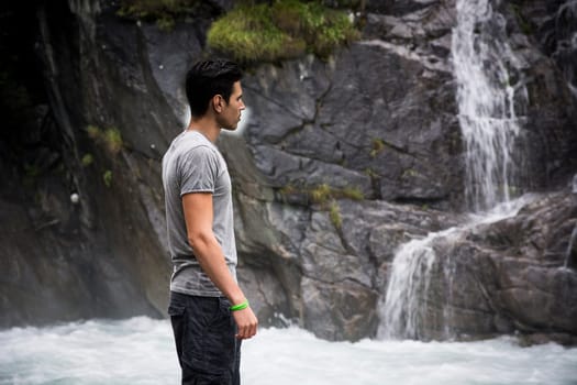 Handsome young man looking at mountain waterfall, profile view.