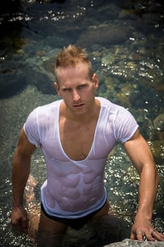 Attractive young bodybuilder by the sea with wet t-shirt on, serious expression