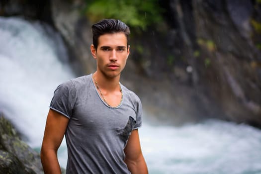 Handsome young man near mountain waterfall looking at camera