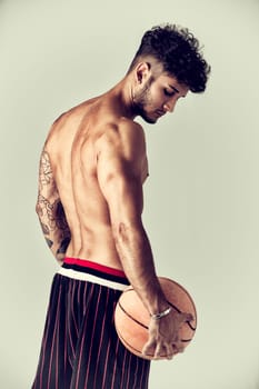 Young athletic man on light background holding basketball ball, back side view