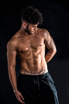 Young athletic man with tattoo posing isolated over black background, studio shot