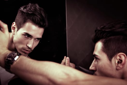 Narcissistic handsome young man leaning forwards admiring his reflection in the mirror in a show of self-absorption