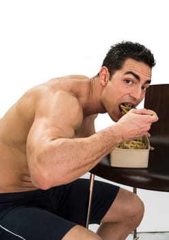 Hungry shirtless muscular young man gulping down food glancing across at the camera without pausing as he takes another mouthful