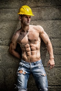 Handsome construction worker standing shirtless in front of a concrete wall