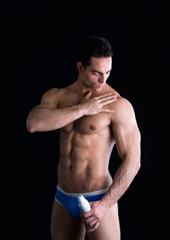 Muscular sexy handsome fit young man wearing a pair of briefs applying ointment from a tube to his shoulder massaging it with a sensual gesture to relieve a strain or injury