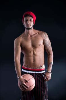 Young athletic man on dark background holding basketball ball, looking at camera
