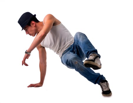 Athletic trendy young man in a hat doing a break dance routine twirling and kicking his foot in the air while balancing on one hand, isolated on white