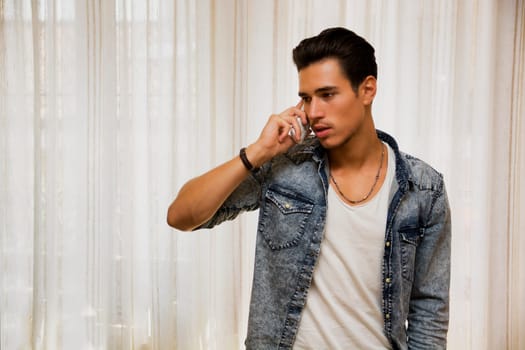 Handsome young man talking on telephone at home, looking to a side