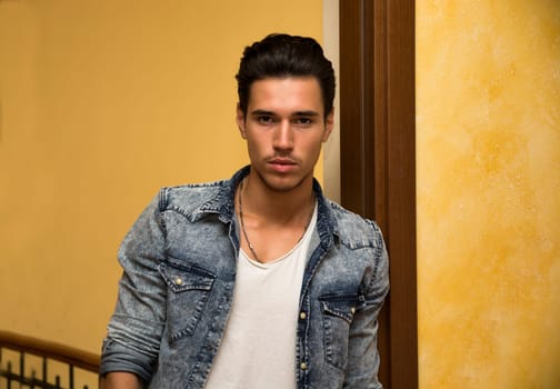 Attractive young man indoors, leaning against door jamb looking at camera