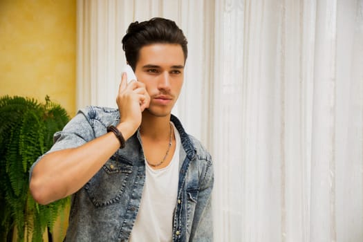 Handsome young man talking on telephone at home, looking to a side