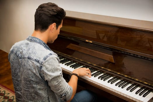 Young handsome male artist playing his wooden classical upright piano, indoor portrait