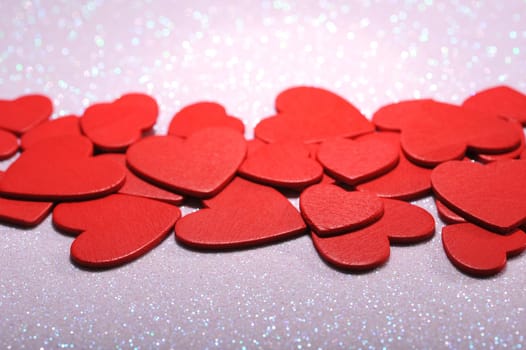 Many small red wooden hearts on a white glitter background