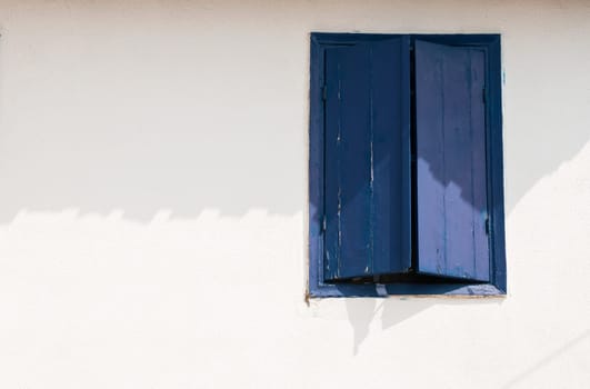 Window with blue wooden shutters on white house wall