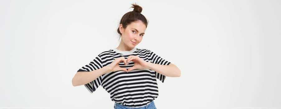 Beautiful european woman, shows heart sign, expresses her love and affection, flirting, standing over white background.