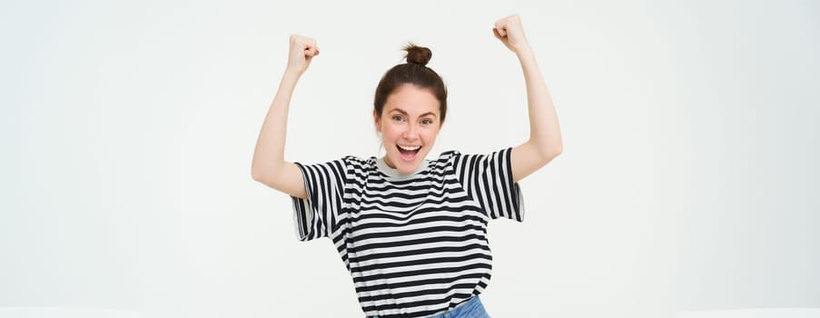 Portrait of happy woman winning, celebrating victory, rooting for team, triumphing, standing over white background.