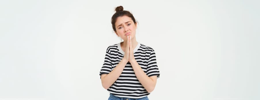 Portrait of sad girl begging you, asking for help, standing in pleading pose, white background. Copy space