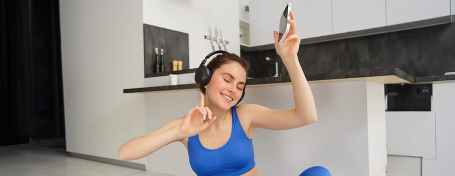 Portrait of young woman in wireless headphones, workout from home, doing fitness exercises, listens music and doing fitness training.