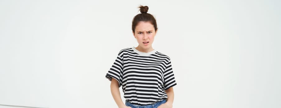 Image of bothered, disappointed young woman, frowning, complaining, looking angry and upset, standing over white background, arguing.