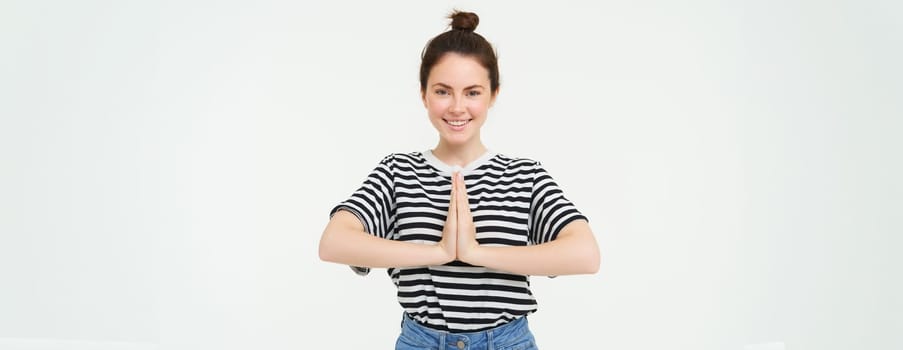 Portrait of beautiful young woman, holds hands together, namaste gesture, say thank you, expresses gratitude, appreciation, stands over white background.