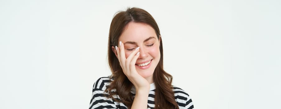 Lifestyle portrait of girl standing over white background, laughing and showing genuine happy emotions.