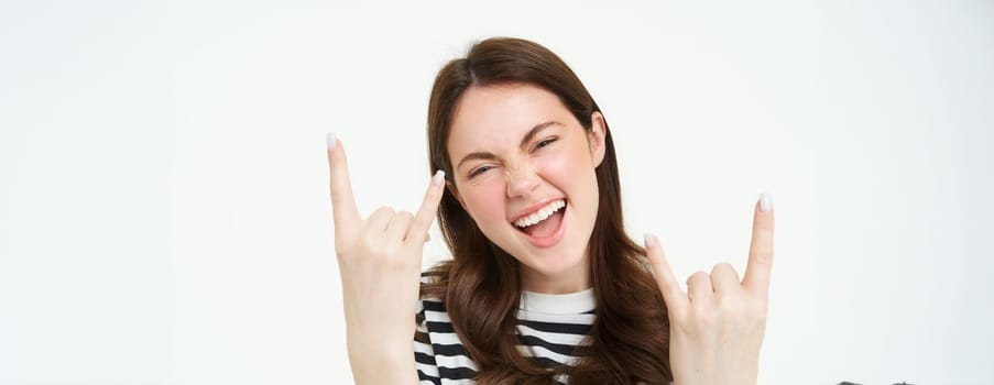 Let it rock. Excited, laughing young woman, showing heavy metal, horns gesture and smiling, having fun, expressing positivity and joy, standing over white background.