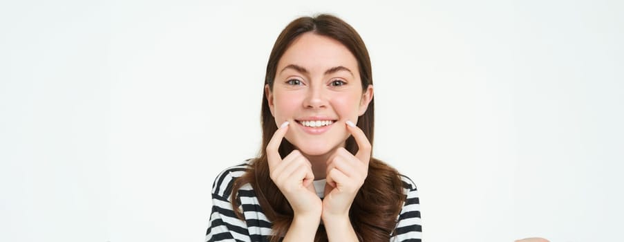 Beauty and women concept. Young smiling woman, showing her cute dimples on face and looking happy, positive emotion, beautiful face without blemishes, standing over white background.